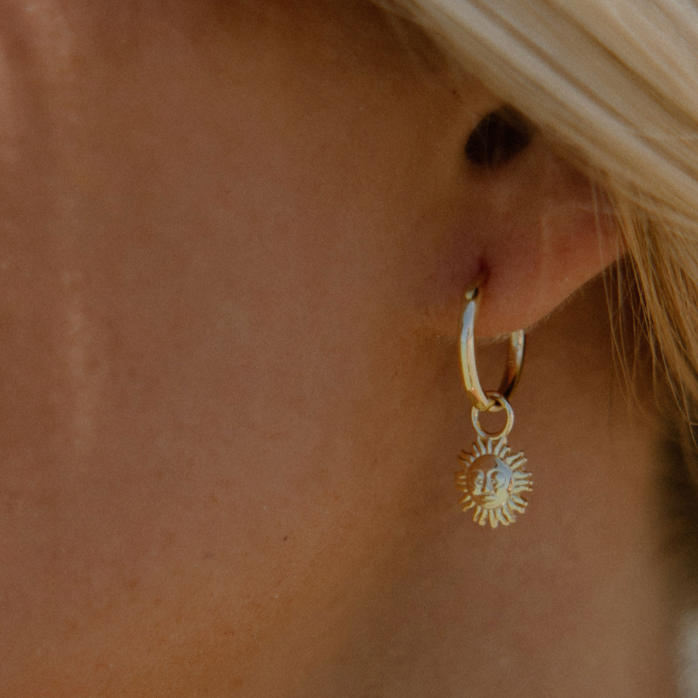 gold hoops engraved with a detailed face of a sun