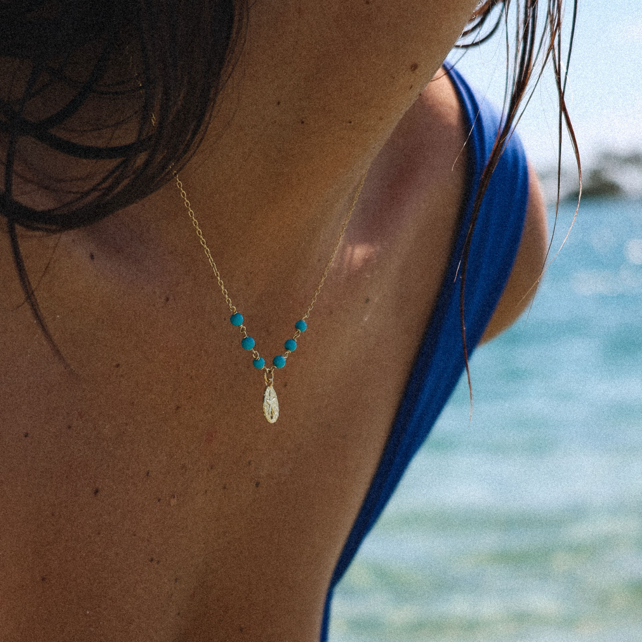 Necklace with turquoise beads and a pendant worn by a person at the beach.