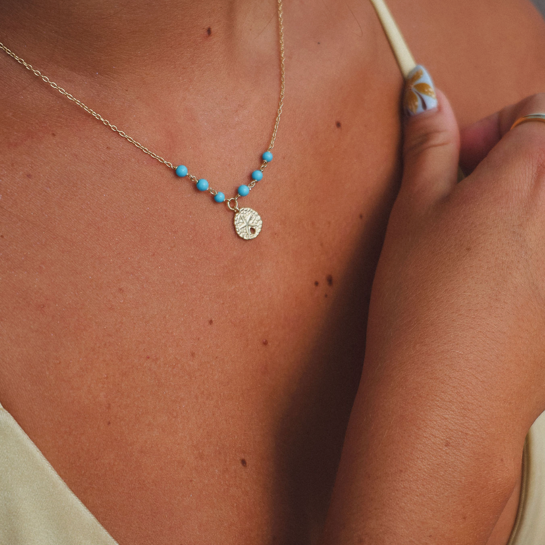 Close-up of a person wearing a gold necklace and bracelet with blue beads.