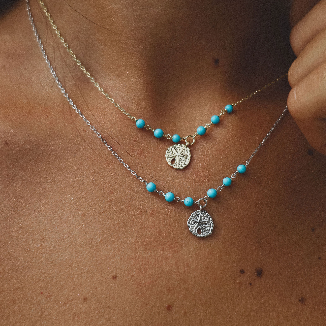 Close-up of a person wearing two necklaces with turquoise beads and sanddollar pendants.