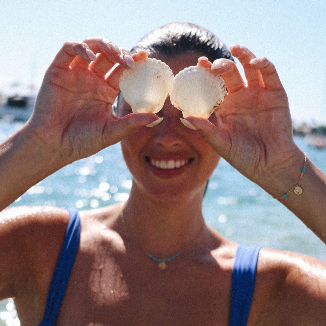 Person holding two seashells over their eyes with a beach background